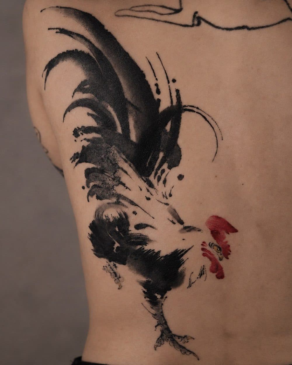 Tattoo of a rooster in black ink brush strokes with a red comb, on a back