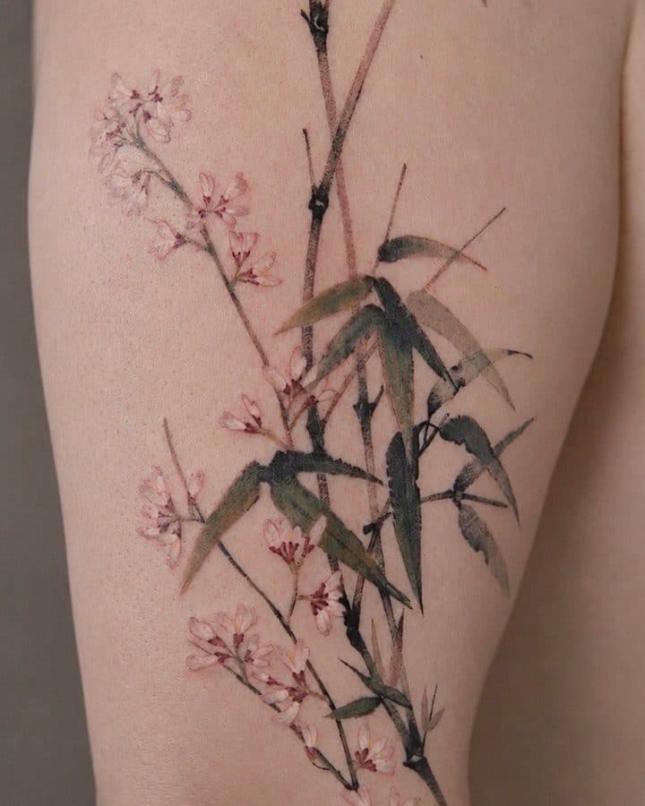 Fine-line tattoo of bamboo stalks with pink blossoms, on a thigh