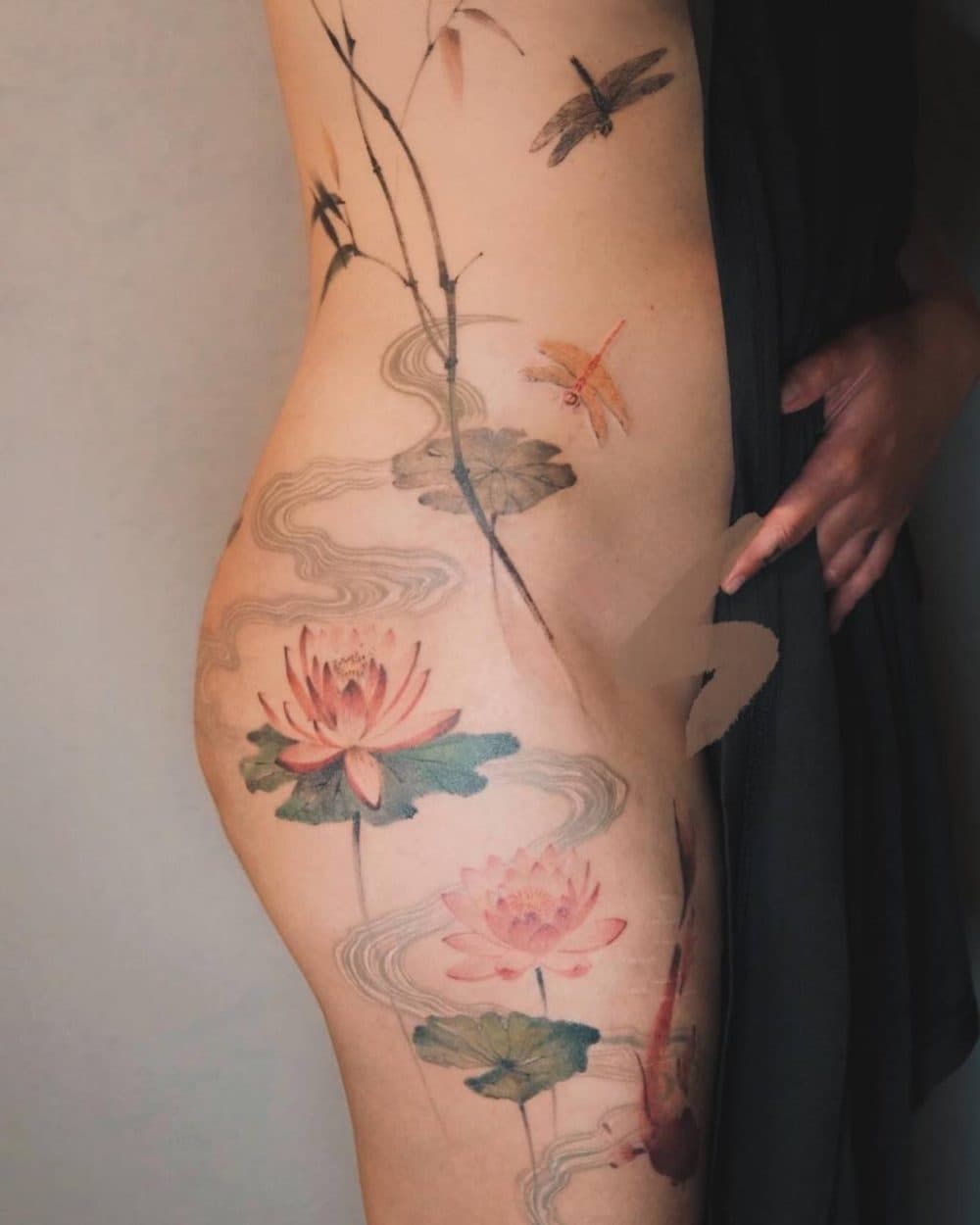 Colour tattoo of lotus flowers, dragonflies and a koi along the side and hip